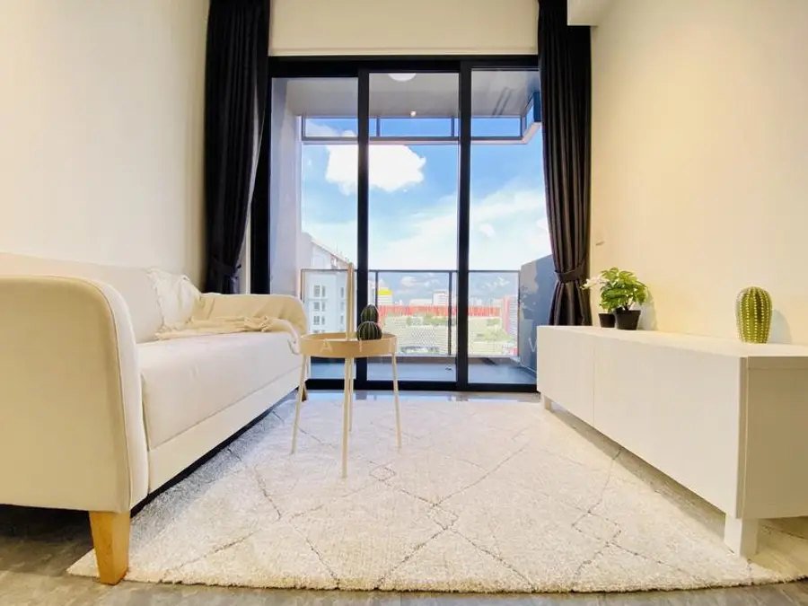 Before, a daytime living room with a white sofa and balcony sliders showing a bright afternoon sky over the city