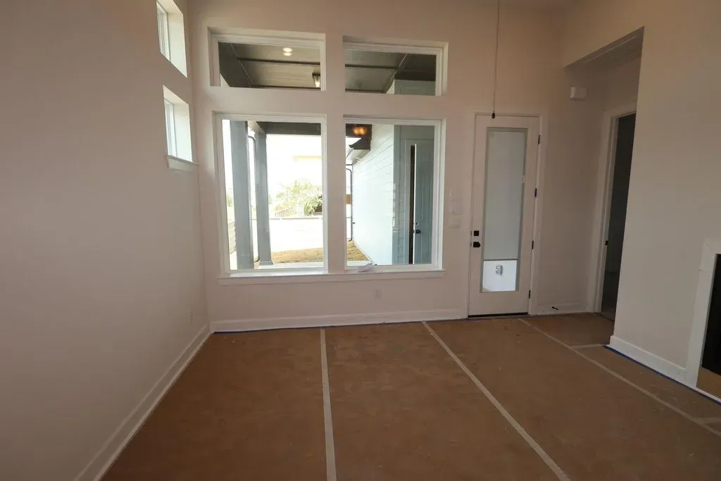Empty new-construction living room before AI virtual staging, with bare walls, transom windows, a glazed side door and brown protective floor covering taped to the subfloor